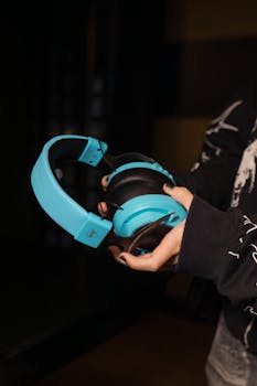 Close-up of a person holding blue headphones with a black background, showcasing modern audio gear.