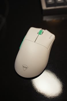 A sleek white wireless mouse with green accents on a shiny black table, perfect for tech setups.