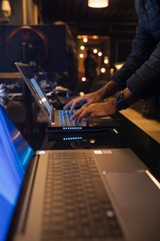 An individual typing on a laptop in a dimly lit modern workspace, emphasizing technology and focus.