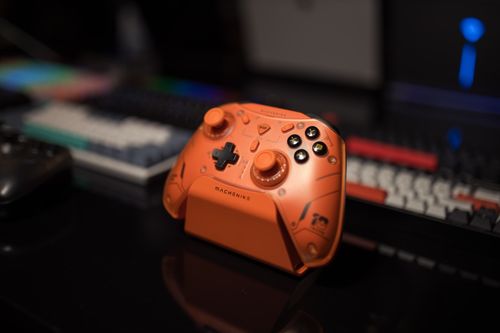 Free Close-up of a vibrant orange gaming controller on a desk with keyboard in background. Stock Photo