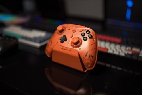 Free Orange gaming controller on black desk with colorful backlit keyboard in background. Stock Photo