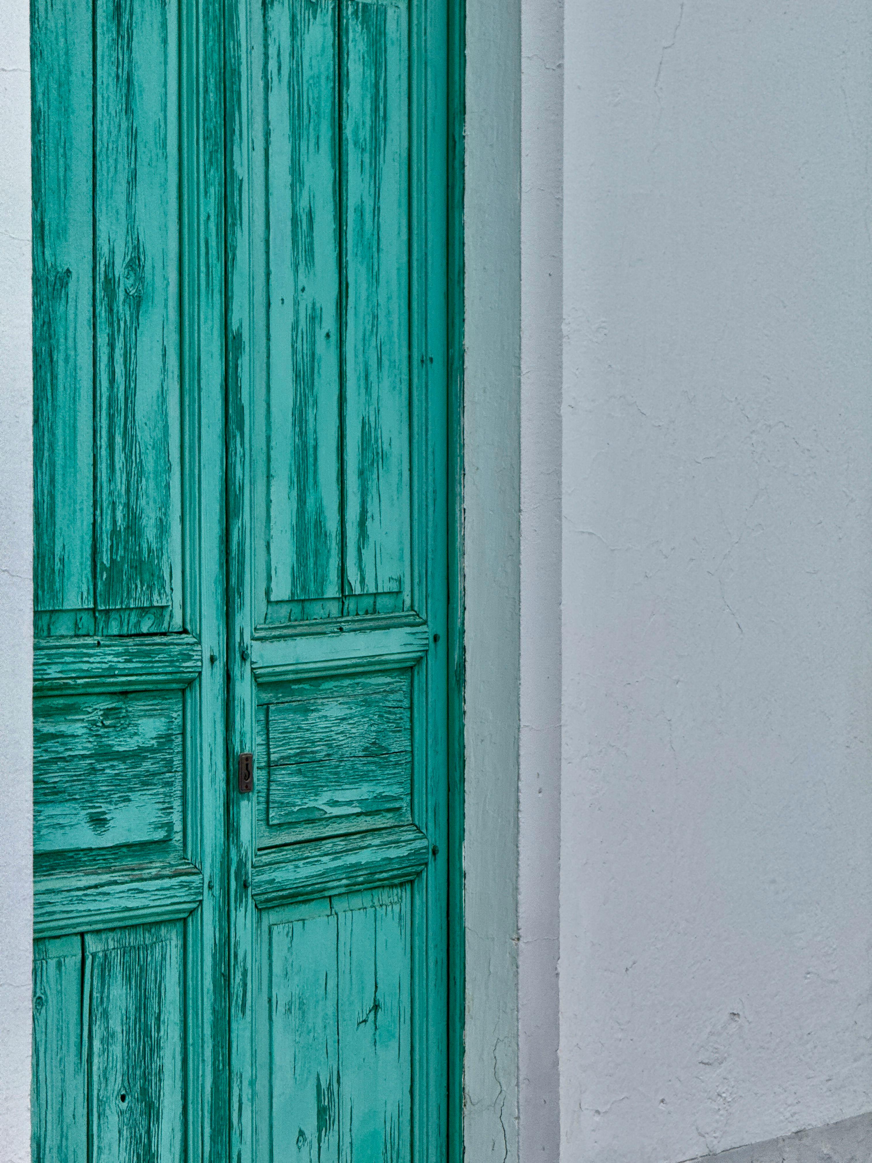 A vintage turquoise door set in a white stucco wall, showcasing rustic charm and vibrant contrast.