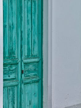 A vintage turquoise door set in a white stucco wall, showcasing rustic charm and vibrant contrast.
