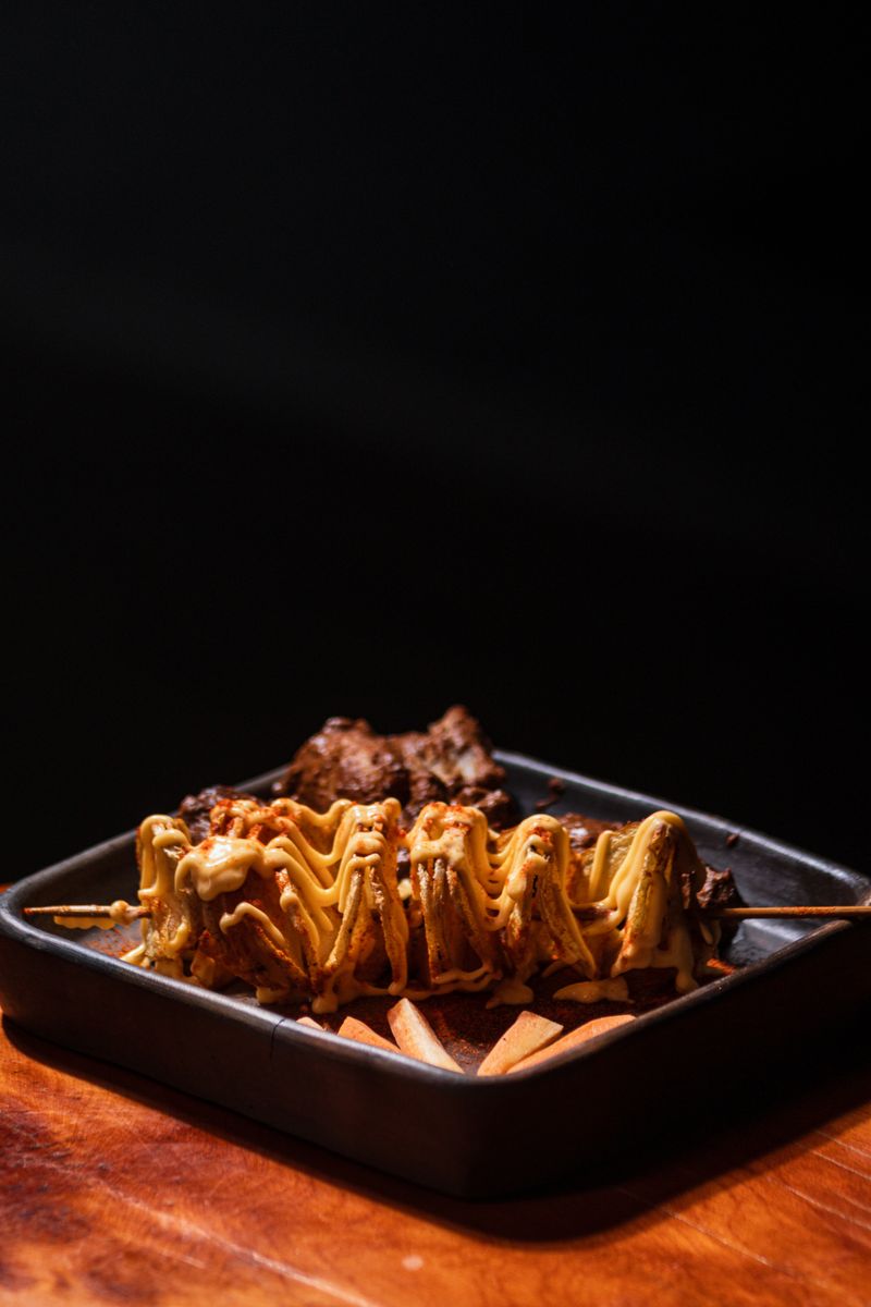 Tasty meat skewers topped with sauce, served with crispy fries in a dark setting.