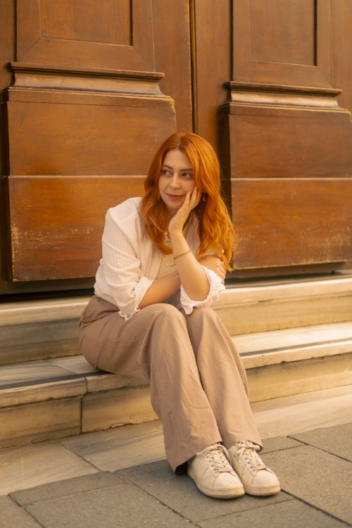 Free A relaxed woman with red hair sits on steps against a wooden backdrop in Istanbul, Turkey. Stock Photo