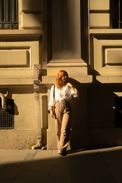 Free A woman with red hair poses in the sunlight against an Istanbul building, showcasing fashion and architecture. Stock Photo
