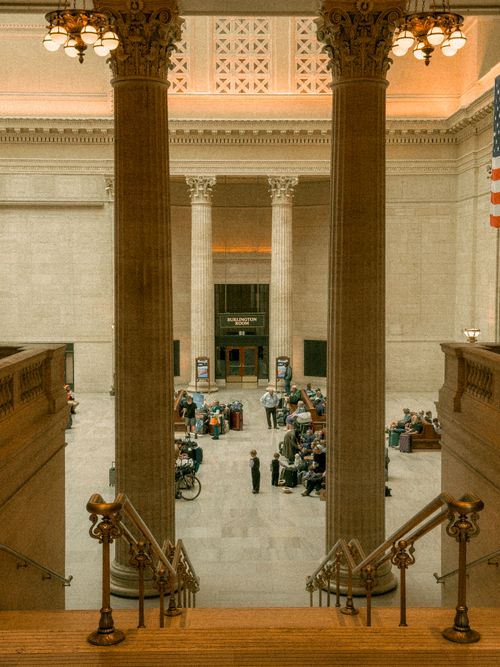 Free Elegant train station hall with grand columns and waiting passengers, offering a classic architectural view. Stock Photo
