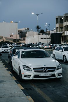 A sleek white Mercedes-Benz CLS parked on a bustling street in Libya during twilight.