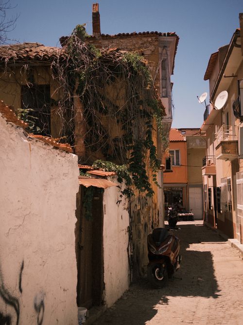Free Old Mediterranean street with ivy-draped walls, scooters, and rustic charm under blue skies. Stock Photo
