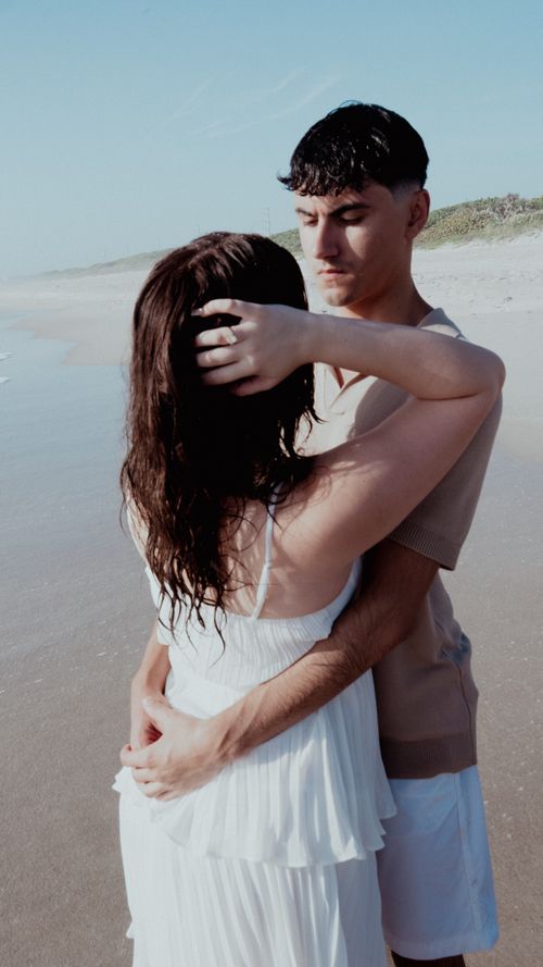 Free A couple sharing an intimate moment by the ocean on a sunny day. Stock Photo