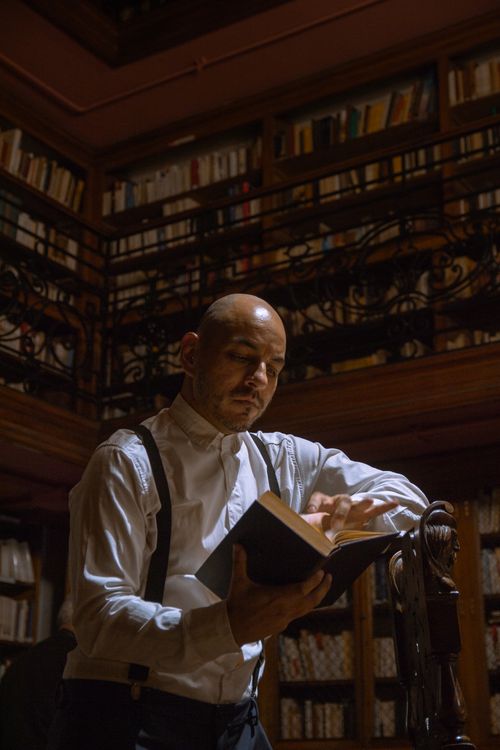 Free A man engrossed in reading a book in a classic, dimly lit library setting, offering a vintage feel. Stock Photo
