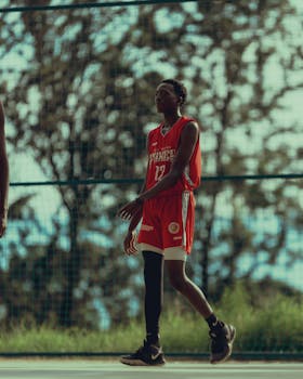 Teen players engage in a dynamic basketball match outdoors in bright sunlight, showcasing teamwork and athleticism.
