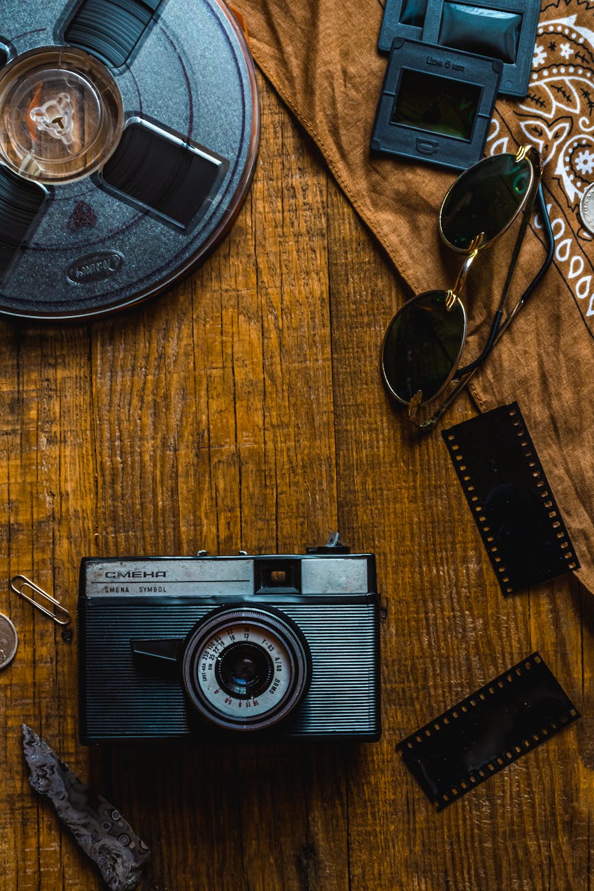 Classic vintage camera surrounded by film reels and negatives on a wooden table for a retro photography theme.