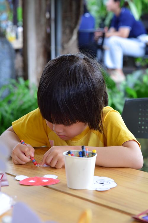 Free Young child focused on an outdoor art activity at a wooden table, crafting with crayons. Stock Photo