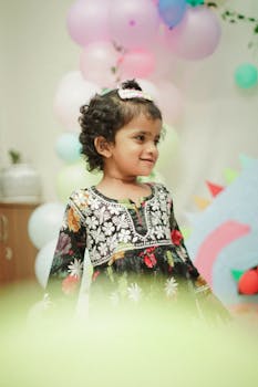 A happy child in a floral dress enjoying a vibrant birthday celebration with balloons and decorations.