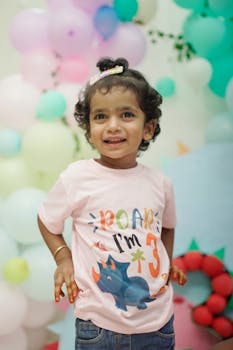 Cute toddler celebrates 3rd birthday with dinosaur theme indoors.