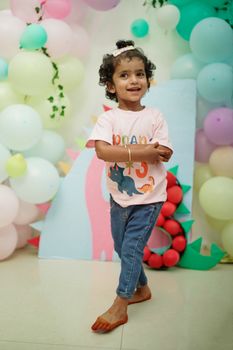 A joyful child at a dinosaur themed birthday with pastel balloons and decorations indoors.