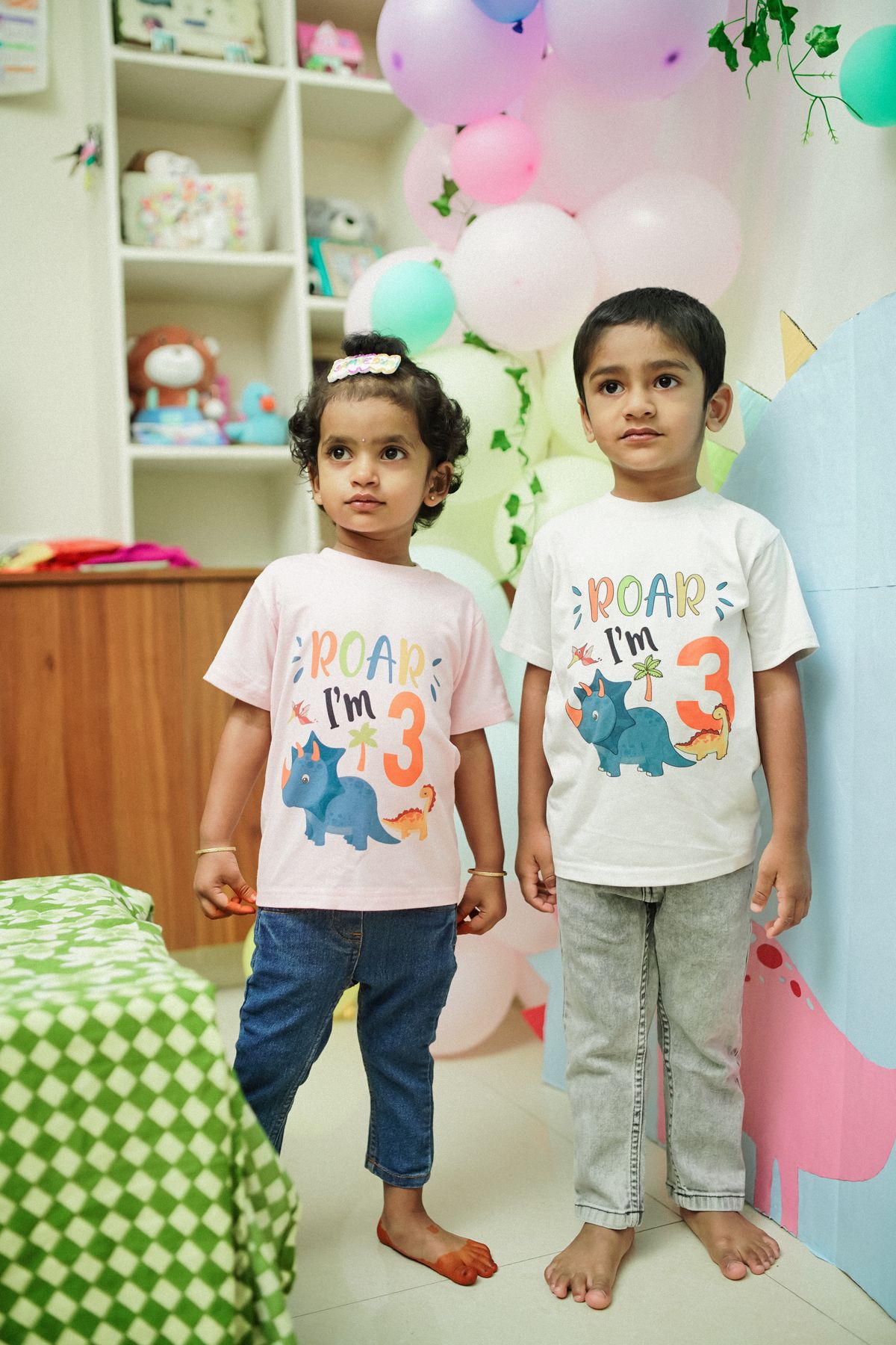 Two children enjoying a dinosaur themed 3rd birthday party with balloons and decoration. Stock Photo.