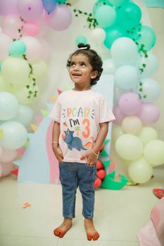 Adorable child at a dinosaur-themed 3rd birthday party with colorful balloons and decorations.