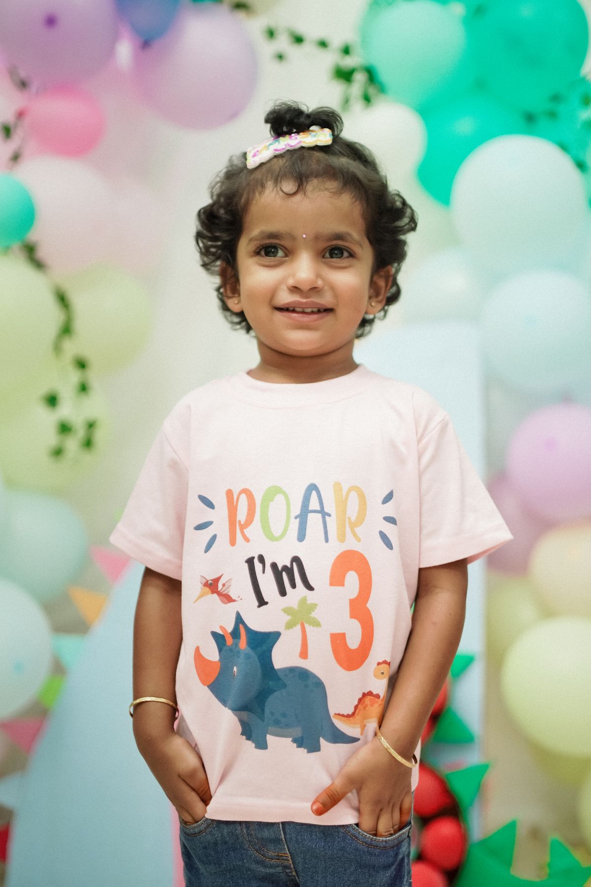 A joyful toddler celebrates her 3rd birthday with a dinosaur theme. Stock Photo.