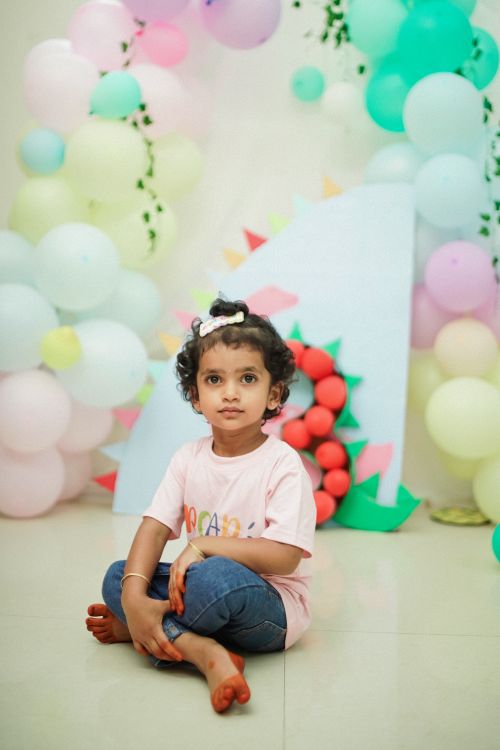 Free Little girl at a dinosaur-themed birthday, surrounded by pastel balloons. Stock Photo