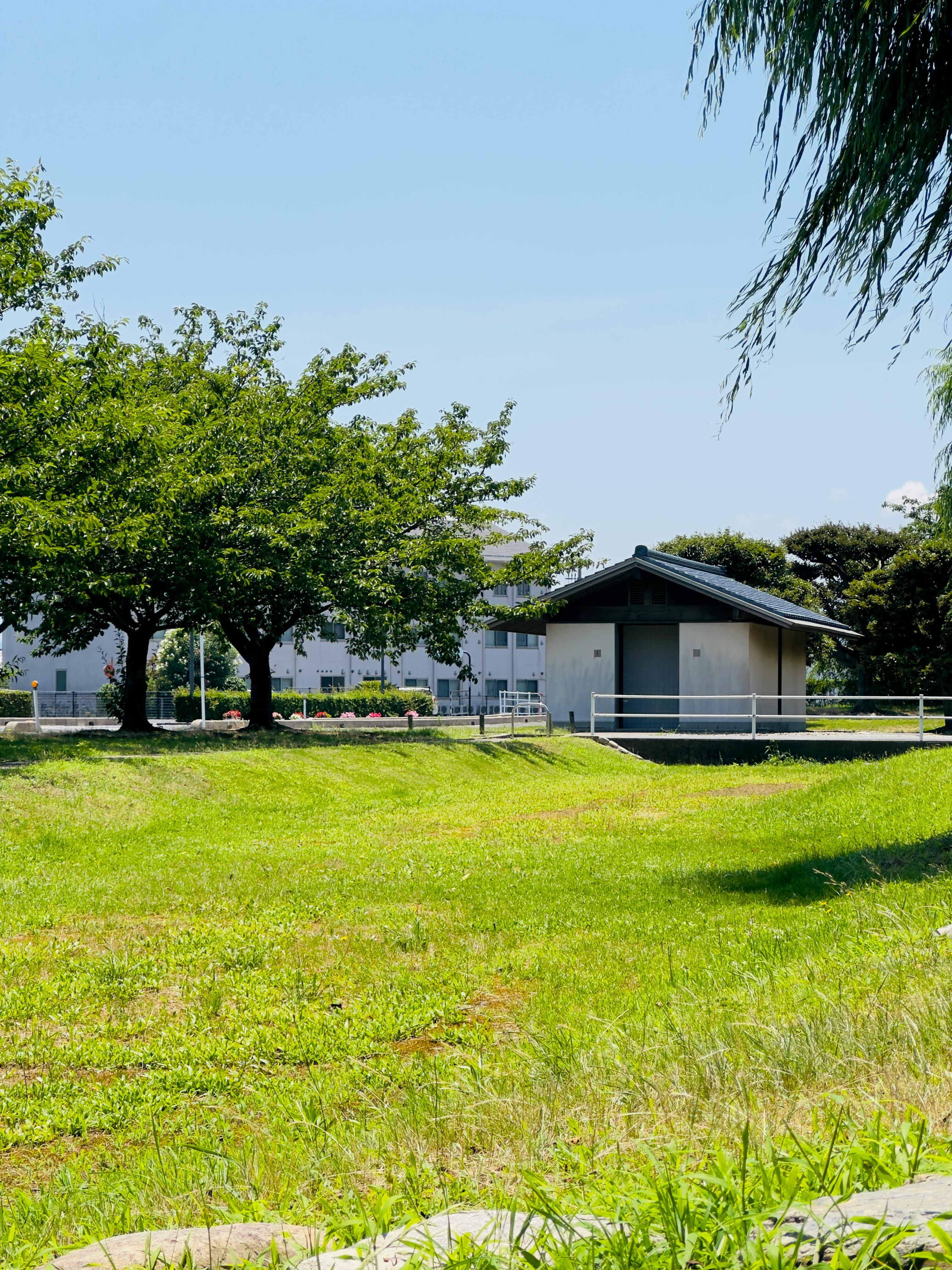 A peaceful park landscape featuring a traditional structure under a clear blue sky.
