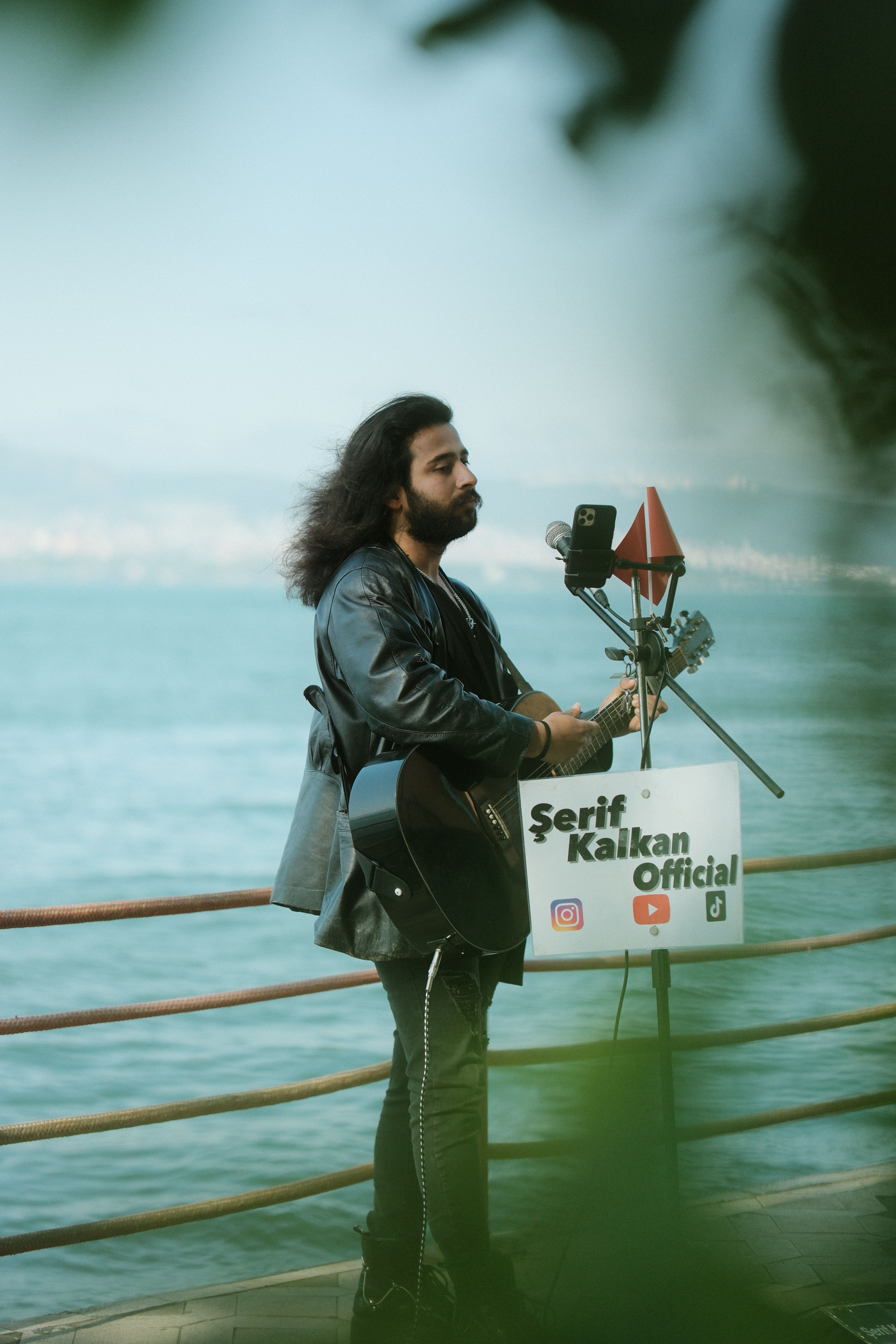 Street musician with black guitar performing by the seaside, creating a serene live music experience.