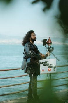 Street musician with black guitar performing by the seaside, creating a serene live music experience.