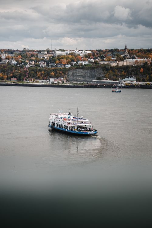 Free Scenic view of a ferry on the St. Lawrence River with Québec City's historic skyline during fall. Stock Photo