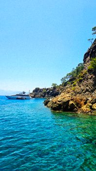 A pristine yacht cruising along a rocky coastline with clear blue waters and vibrant landscape.
