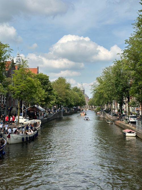 Free Beautiful Amsterdam canal with boats and lush greenery under a bright sky. Stock Photo