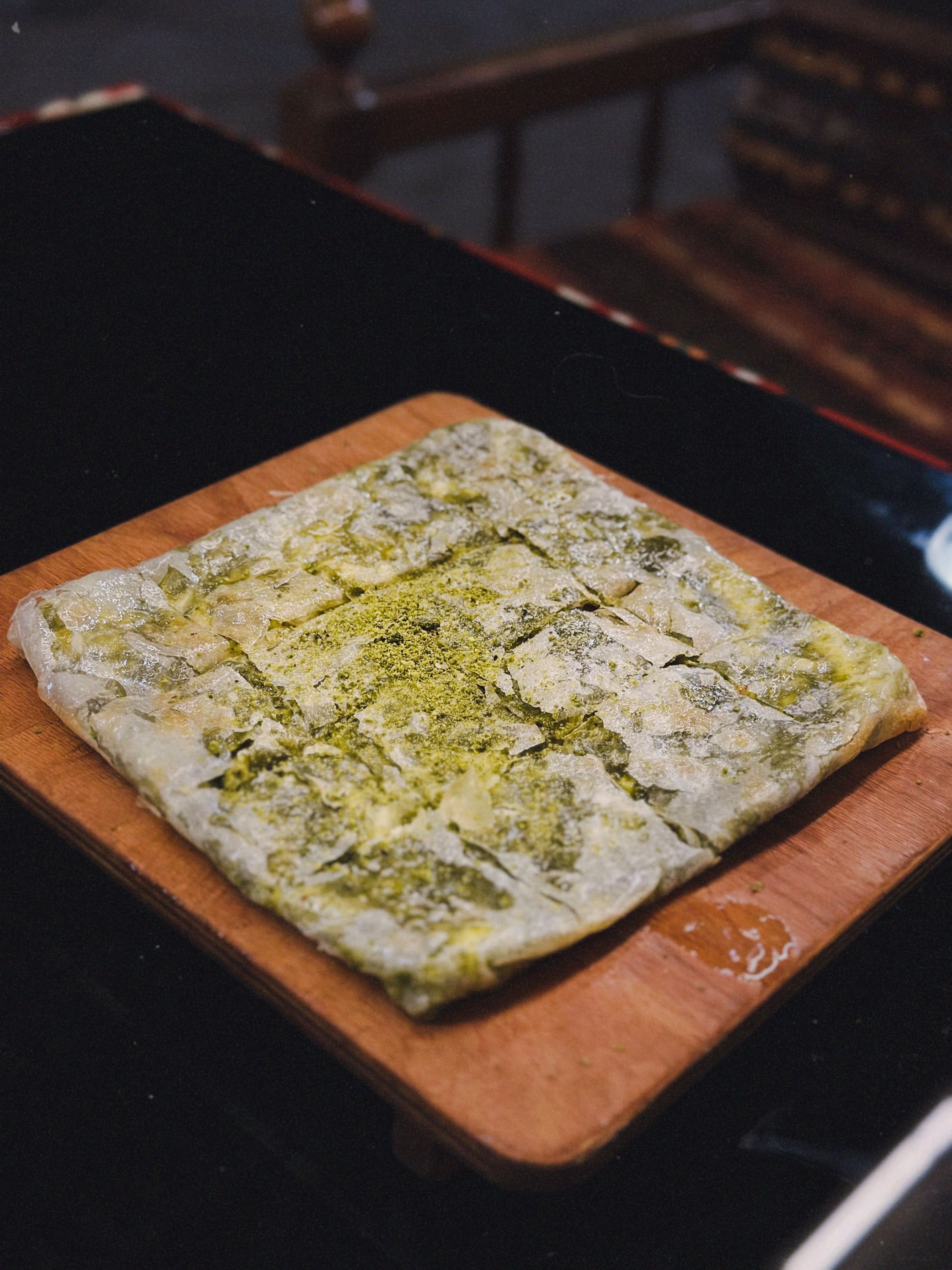Square pistachio baklava dessert on a wooden board, perfect for culinary or dessert themes.