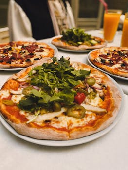 A tempting display of four assorted pizzas topped with fresh vegetables and greens, perfect for sharing.