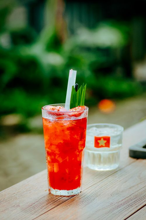 Free Vibrant red cocktail with straw on a wooden table outdoors, with a green lush background. Stock Photo