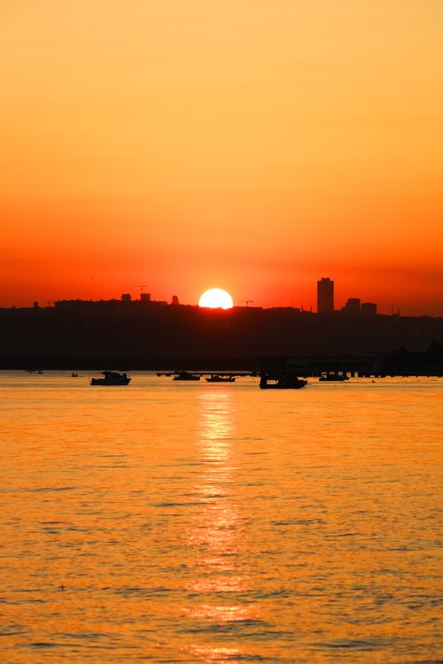 Free Golden sunset reflecting over calm water with silhouette of city skyline and boats. Stock Photo