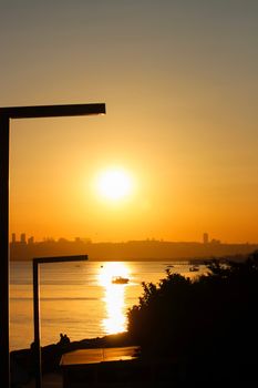 A mesmerizing golden sunset casts warm hues over a calm river, with silhouetted cityscape in the distance.