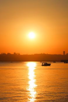 A tranquil sunset casting a golden glow over calm waters with a boat silhouette.