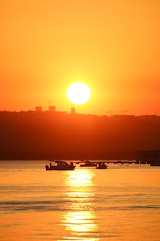 Beautiful golden sunset over calm waters with silhouetted boats creating a serene atmosphere.