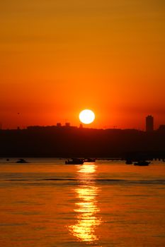 Stunning sunset with golden hues reflecting on tranquil waters, featuring boats on the horizon.