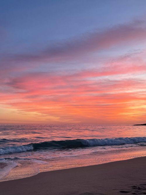 Free Golden sunset over ocean waves and sandy beach with vibrant pink sky. Stock Photo