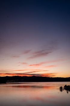A breathtaking sunrise over a calm lake with vibrant colors reflecting on the water creating a peaceful ambiance.