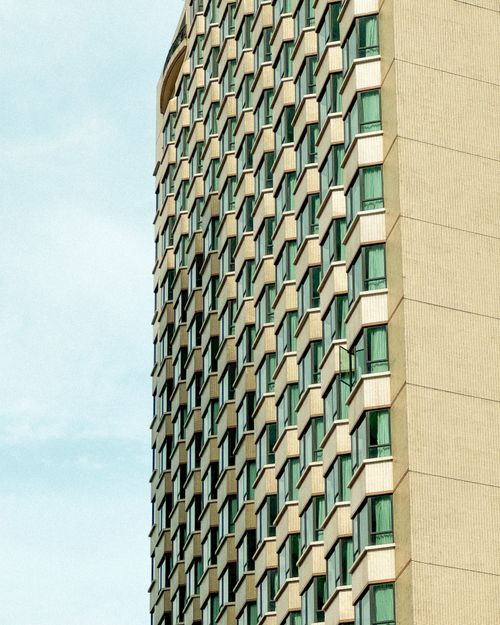 Free Close-up view of a modern high-rise building facade with geometric design under a clear blue sky. Stock Photo
