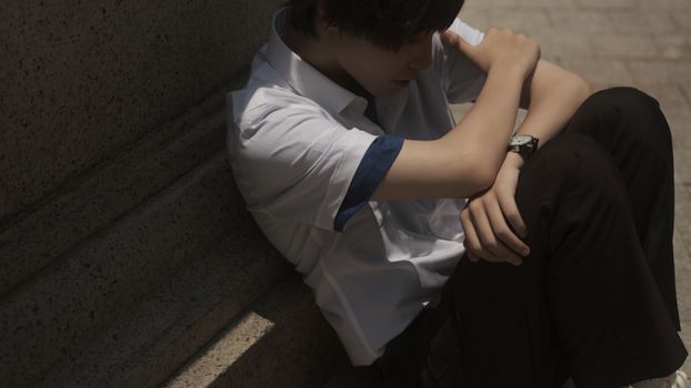 Teenager sitting thoughtfully on concrete steps, casting a shadow.