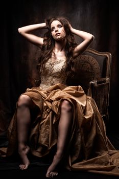 A woman in an elegant gown sits on a vintage chair, displaying grace and luxury.