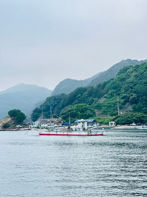 Free Tranquil fishing boat on calm waters surrounded by lush green hills and cloudy sky. Stock Photo