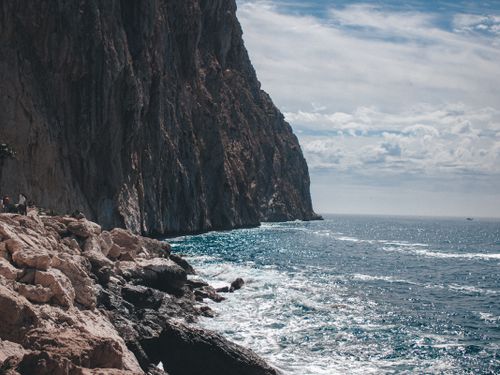 Free Majestic cliffs towering over a sparkling blue ocean under a partly cloudy sky. Stock Photo