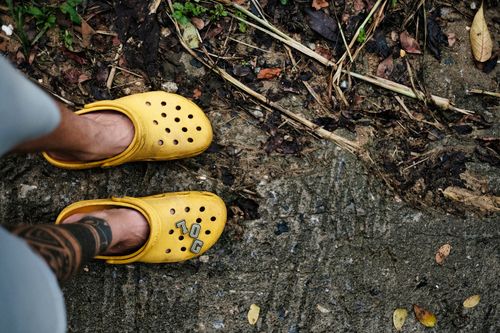 Free Man in yellow Crocs with tattoo on foot standing on earthy path with dried leaves. Stock Photo