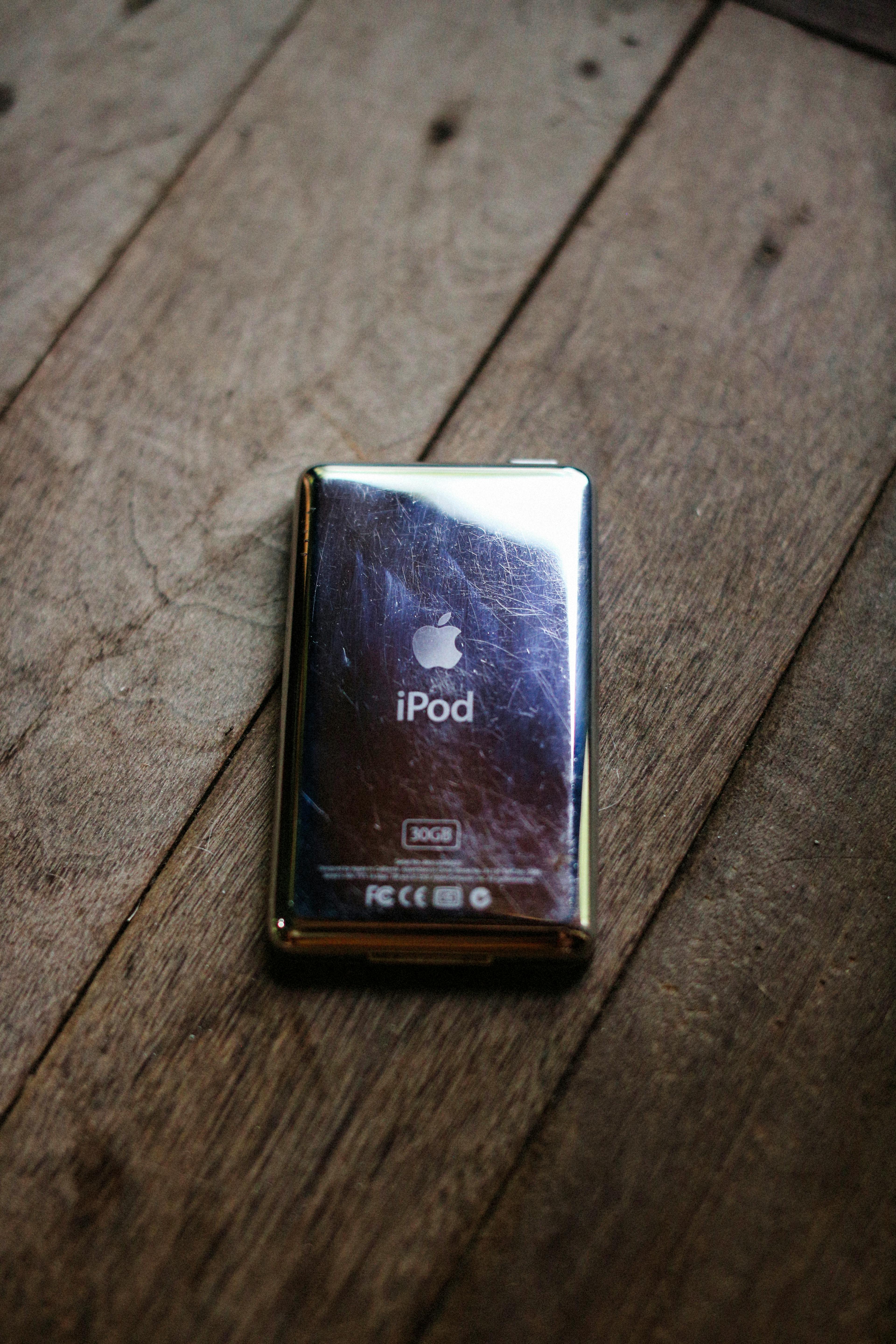 Classic iPod 30GB with a reflective surface on a rustic wooden floor.