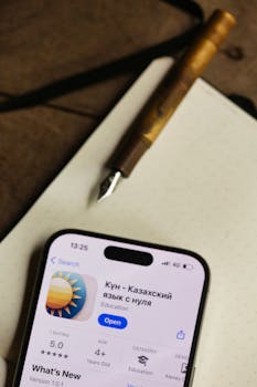 Discover the Kazakh language learning app on a smartphone next to a classic fountain pen and notebook.