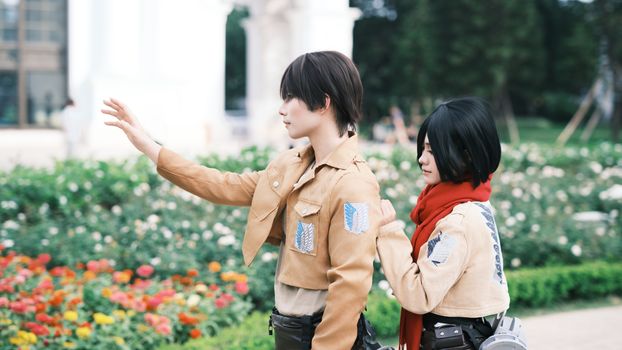 Two cosplayers dressed in anime costumes posing in a colorful garden.